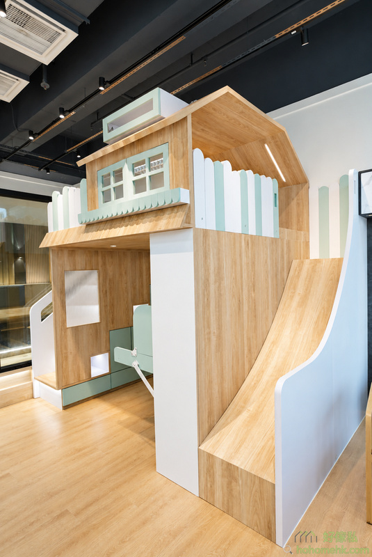展示廳內訂造兒童高架閣樓床全景，淺木紋夾板配薄荷綠飾面，右側設弧形滑梯，上層為小屋造型睡眠區，下層為書房兼遊戲區，頂部設天花射燈，整體清新北歐風格