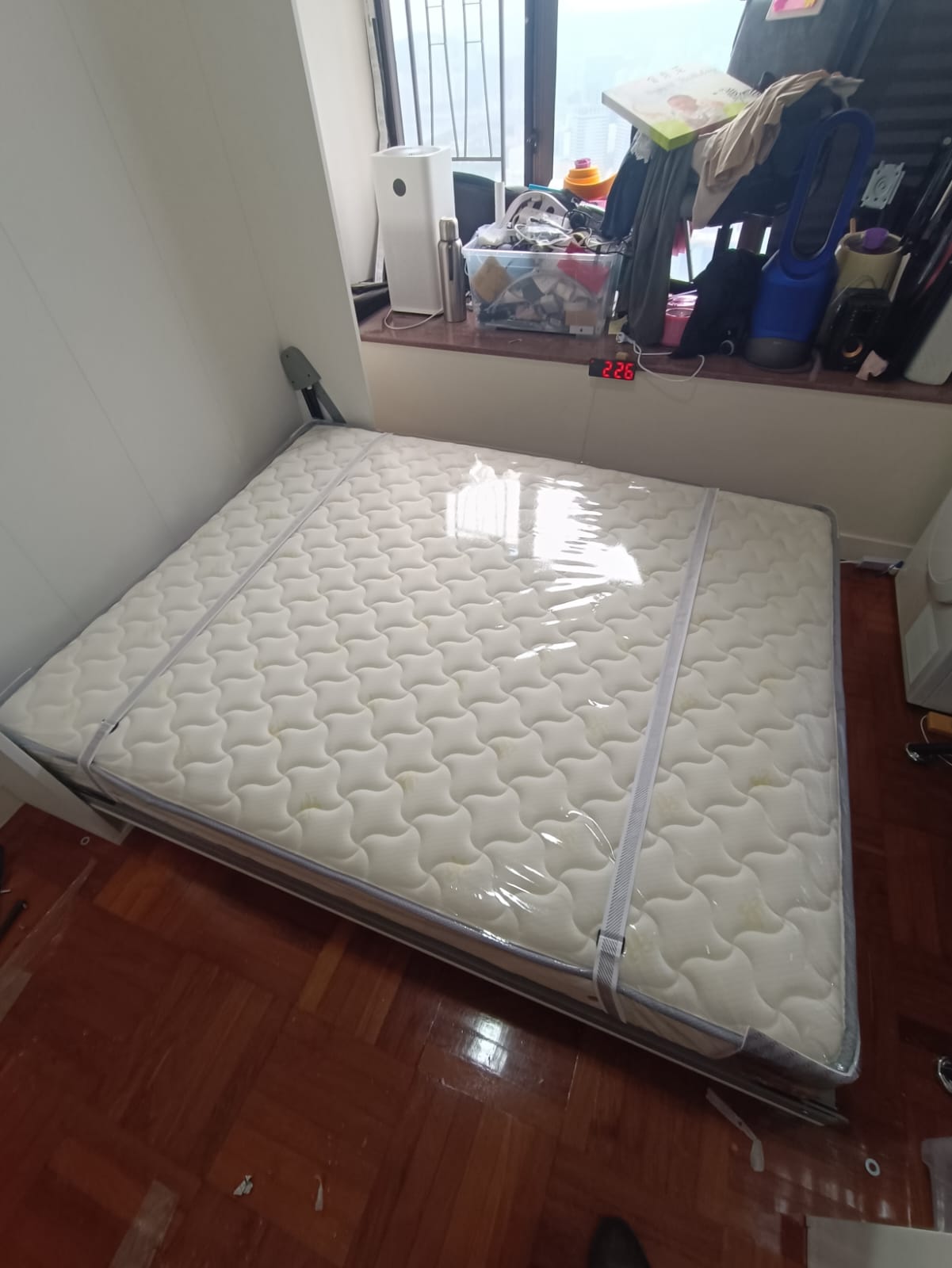 從上方拍攝已打開的白色5尺直翻床，白色波浪紋床褥置於框架內，兩條固定帶沿床身伸展，床尾靠近木地板通道。