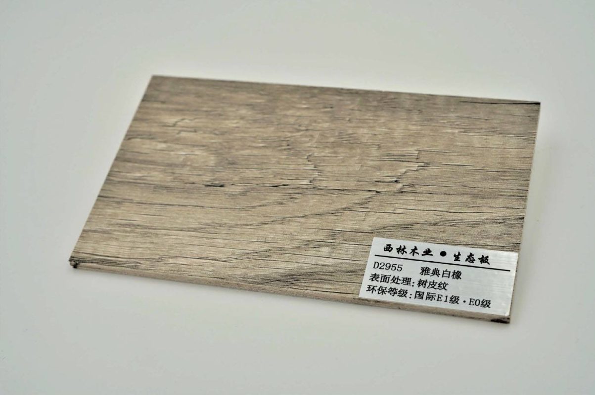 木業生態板物料樣板近攝，淺灰白色底調帶天然樹皮紋路，右下角標籤顯示「西林木業生態板 D2955 雅典白橡，表面處理：樹皮紋，環保等級：國際E1級·E0級」，板邊可見多層夾板結構截面。