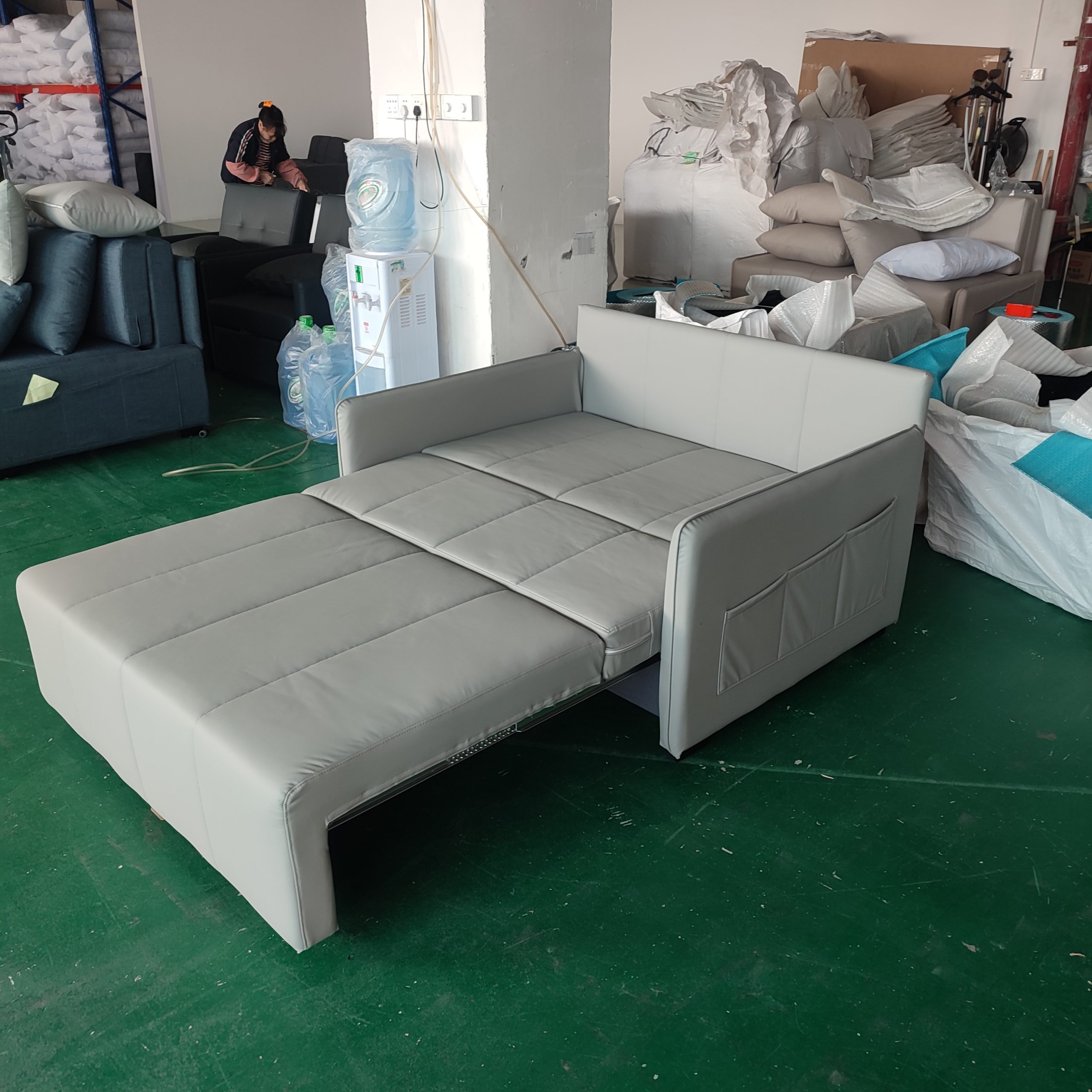 Takumi 6079款淺灰色貓抓科技皮梳化床拉出床舖斜側俯視，床面平坦以橫向縫線分三段，靠背及扶手可見皮革包覆，工廠環境，後方有工作人員及其他傢俬