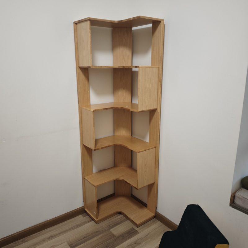 原木色Peyton五層轉角書架擺喺兩幅白牆夾住嘅角位，地板係啡色橫紋木地板，右邊角落隱約見到黑色椅腳同綠色小盆栽，層板暫時空置。