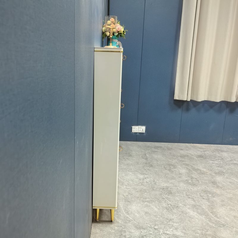 Caleb 超薄鞋櫃工廠實拍正側面獨立影，櫃身薄身輪廓由地面延伸至頂，頂面擺一支金色燭台襯乾花，金色細腳架起底部，右邊見到淺灰窗簾同雙插座位，深藍色牆身同深灰石紋地板。