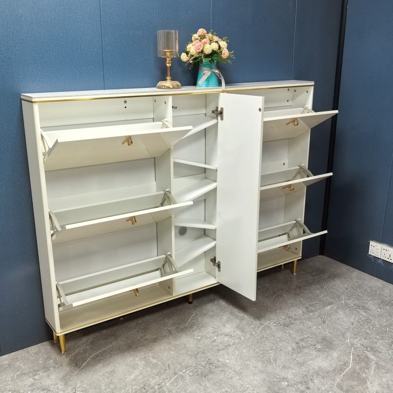Caleb160cm闊鞋櫃工廠實拍，米白色亮光烤漆機身，左右兩邊各三格翻斗全開展示斜面隔板，中間直立紋理門打開露出多層平面層板，頂部擺放金色枱燈同粉色花藝，深藍牆身背景。