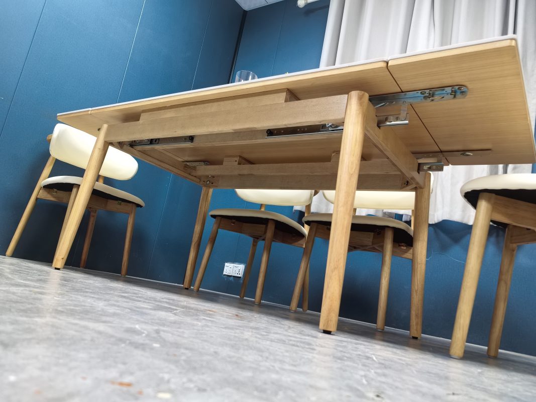 低角度側拍正在展開的Reese岩板伸縮餐枱，右側加長枱板向外伸出，枱底可見金屬滑軌、承托件及原木色實木框架。