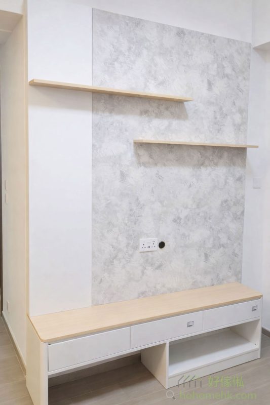 客廳採用淺灰石紋與白色作主調，給人一種清新且充滿現代感的視覺效果。電視背板運用了簡潔的線條設計，搭配木紋層板，不僅提升了儲物功能，還增添層次感。全白的矮櫃設計，與淺灰石紋牆面形成對比，令整體空間更為輕盈明亮。