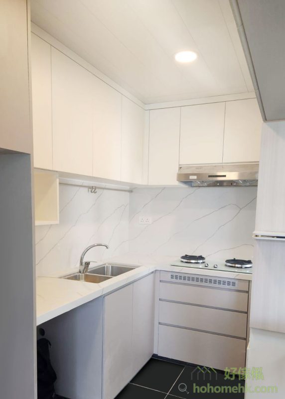 廚櫃、浴室櫃及客廳、睡房的訂造傢俬均採用相同的材質及設計風格，令整個單位的視覺效果顯得更為統一。無論是廚房的潔白牆身，還是浴室的簡約線條，每一件訂造傢俬都體現了細緻的工藝。開放式廚房選擇灰杏色和大面積的奶油色，使整個客廳空間顯得更寬敞光亮。