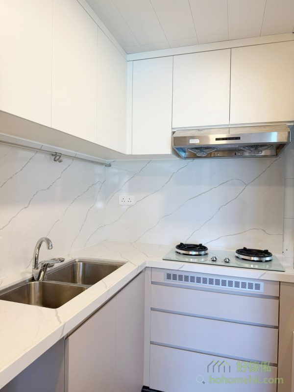 廚櫃、浴室櫃及客廳、睡房的訂造傢俬均採用相同的材質及設計風格，令整個單位的視覺效果顯得更為統一。無論是廚房的潔白牆身，還是浴室的簡約線條，每一件訂造傢俬都體現了細緻的工藝。開放式廚房選擇灰杏色和大面積的奶油色，使整個客廳空間顯得更寬敞光亮。