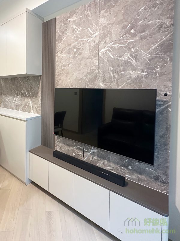 電視背景牆選用了粗獷的石紋元素作為設計主角，視覺效果搶眼卻不顯花巧，與客廳整體色調完美融合。配搭懸空電視地櫃的設計，讓背景牆的橫樑底部騰出空間安裝燈帶，柔和的滲光效果為家居增添一份溫馨氛圍。