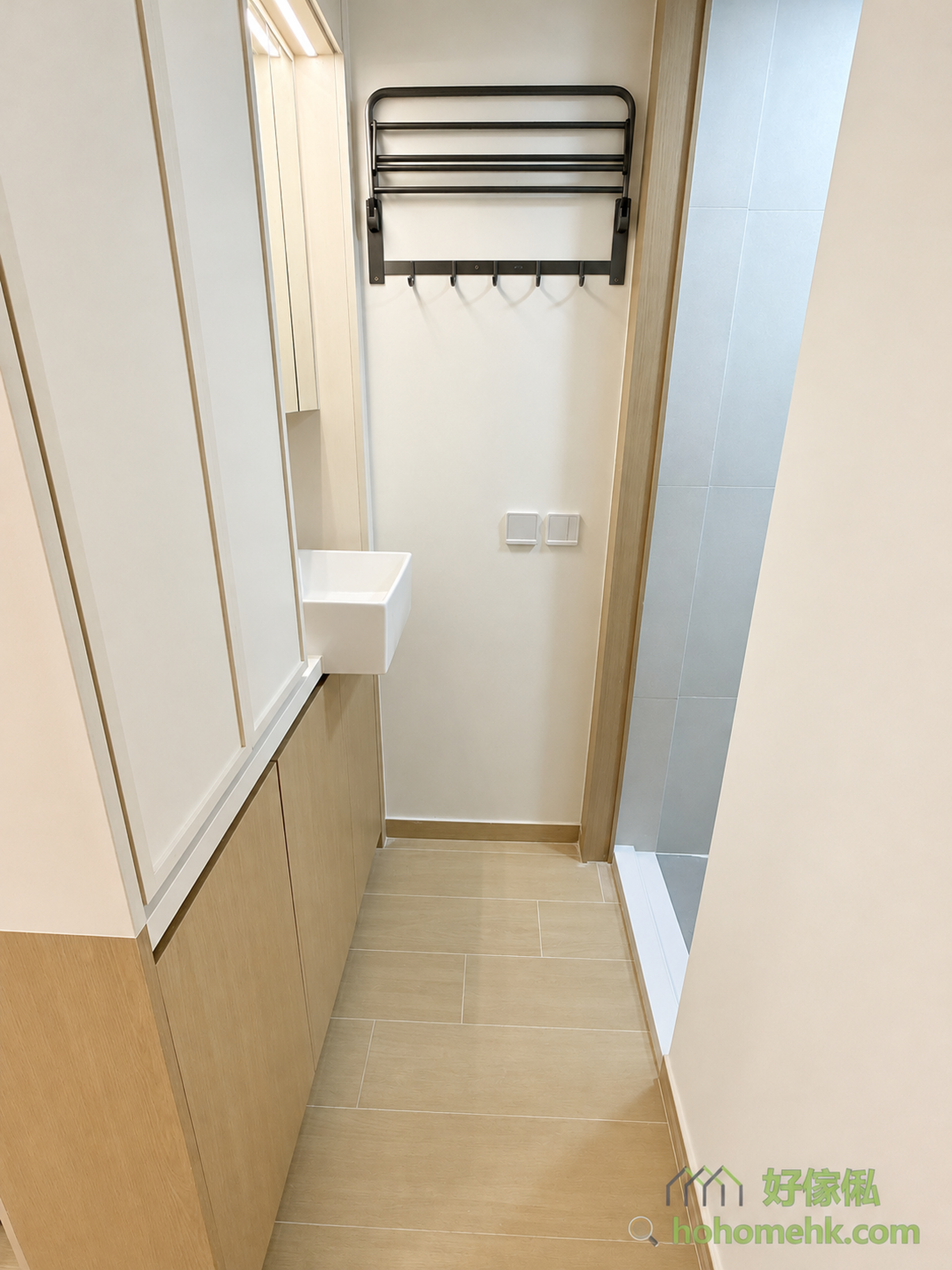 觀塘順天邨公屋裝修改造，走廊盡頭可見白色洗手盆移出廁所外，左側設白色鏡櫃，牆上掛金屬毛巾架連掛鉤，右方可見藍色瓷磚廁所入口，地板鋪米色石紋地磚，整體日系簡約風格。