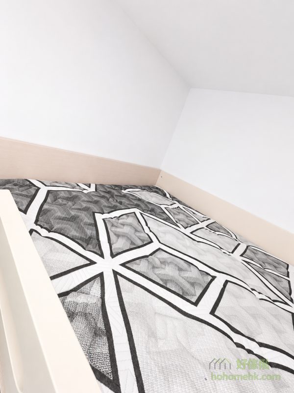 高架床睡眠區近鏡，床位設於白色房間牆角，灰白色幾何圖案床品鋪滿床面，淺木色床板沿牆身包邊，前方可見淺米色床邊板。